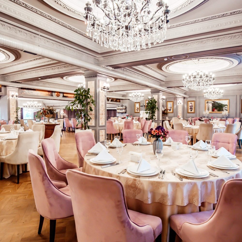 restaurant hall with round and square tables some chairs and plants